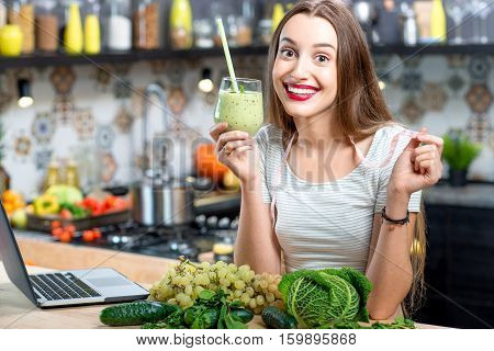 Portrait of young smiling woman with green smoothie in the kitchen at home. Healthy vegetarian diet for weight loss and detox