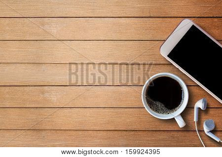 Cup of coffee with smart phone and earphone on wood table background with copy space for any design. smart phone and coffee cup on wooden top view