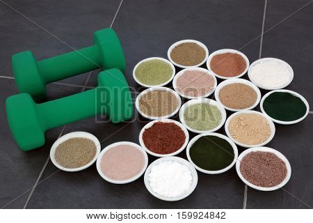 Body building supplement powder and dumbbell weights in porcelain bowls over slate background.