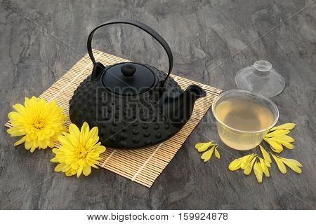 Chrysanthemum flower tea with flowers, oriental teapot and glass cup with lid on bamboo mat. Also used  in traditional chinese herbal medicine.