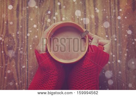 Woman holding cup of hot cacao or coffee on wooden background Closeup of hands in warm red sweaters. Top view. Toning image.