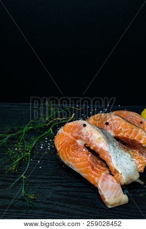 Slices Of Red Fish Salmon On Trout With Lemon, Dill, Pink And White Salt, On Black Wooden Background
