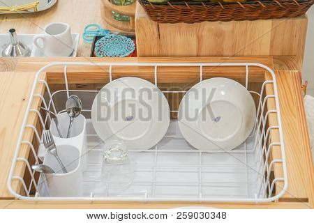 Clean Ceramic Dish And Stainless Cutlery Set In Plastic Drainer After Washing