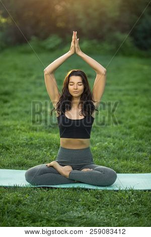 Young Girl Doing Yoga In The Park. Woman Practicing Yoga, Stretching In Lotus Position Outdoors With