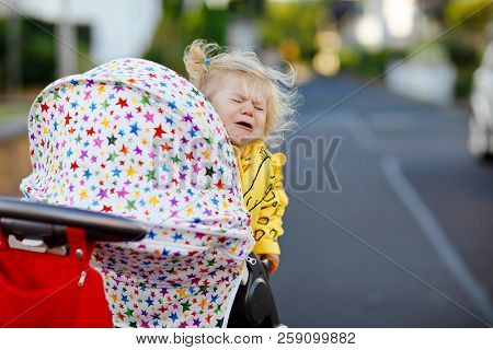 Portrait Of Little Sad Toddler Girl Sitting In Stroller And Going For A Walk. Crying Baby Child Does