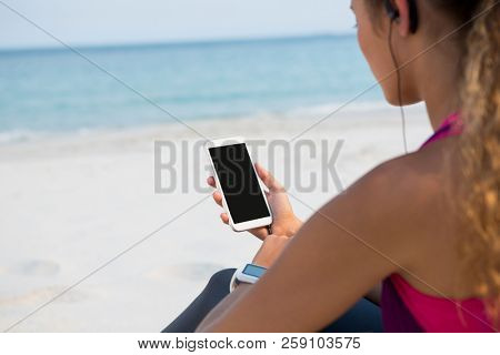 Mid section of woman using mobile phone while sitting at beach against sky