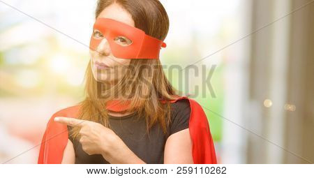 Middle age super hero woman wearing red mask and cape pointing away side with finger