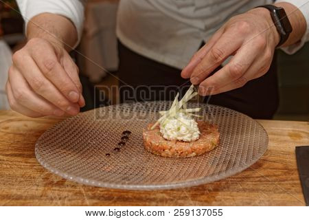 Professional chef is decorating salmon tartar with cut apple and whipped cheese cream