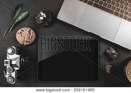 On A Black Stone Table Is A Laptop For Work, A Photo Camera, A Graphic Tablet And Sweets. Top View, 