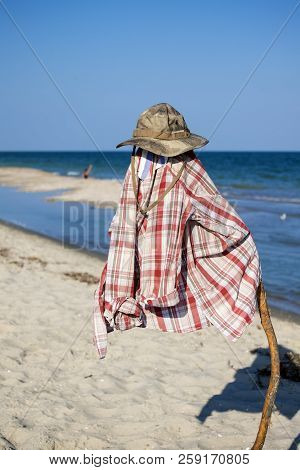 Camouflage Hat And Checkered Shirt On A Pole Against The Backdrop Of A Seaboard And The Blue Sea