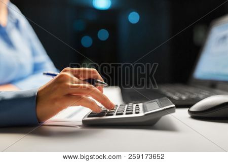 business, finance and accounting concept - close up of businesswoman with calculator counting and filling tax form at night office