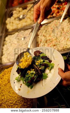 Customer Of A Self-service Restaurant Serves Its Dish With Corn And Lettuce