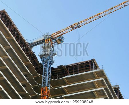 Construction Site. Concrete Building Under Construction. Crane And Building Against Vlue Sky.