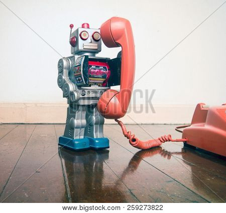 big silver robot toy on  a  retyro  phone standing on an old wooden floor toned image