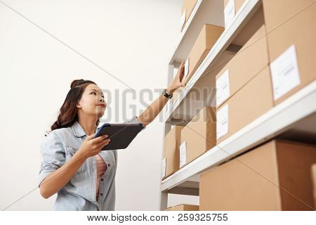 Asian Postwoman Checking Parcels With Digital Tablet At Storehouse