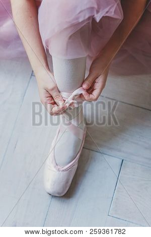Hands Of Ballerina In Pink Tutu Skirt Puts On Pointe Shoes On Leg In White Light Hall. Young Classic