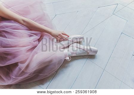 Hands Of Ballerina In Pink Tutu Skirt Puts On Pointe Shoes On Leg In White Light Hall. Young Classic