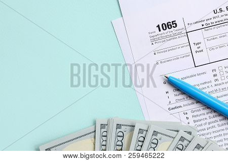 1065 Tax Form Lies Near Hundred Dollar Bills And Blue Pen On A Light Blue Background. Us Return For 