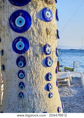 A Lot Of Nazar Boncugu, A Turkish Eye-shaped Amulet Screwed To A Tree With The Aegean Sea In The Bac