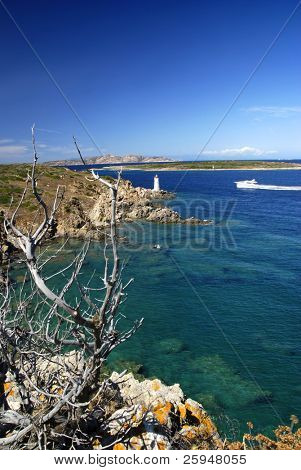 Phare sur roches Sardes et un yacht naviguant dans la mer