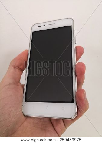 Hand Holding A Mid-range Economic White Smartphone. Cell Phone With Black Screen Isolated On White B