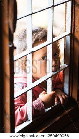 GHALEGAUN, NEPAL - CIRCA MAY 2018: Young Nepali girl looking through an open window with grill.