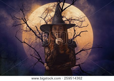 Halloween Witch Showing Silence Sign With Finger Over Lips Standing Over Dead Tree, Full Moon And Sp