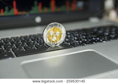 Golden And Silver Ripple Coin On A Black Keyboard Of Silver Laptop And Diagram Chart Graph On A Scre