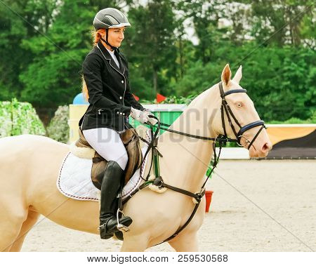 Beautiful Girl And Horse In Jumping Show, Equestrian Sports. Isabelline Akhal-teke Mare With Blue Ey