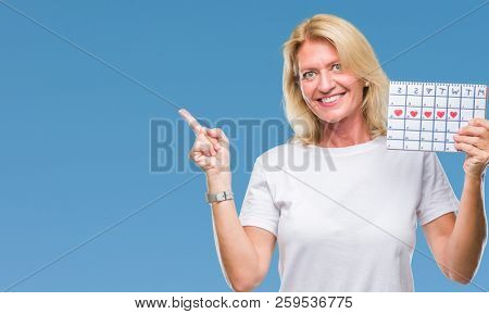Middle age blonde woman holding menstruation calendar ver isolated background very happy pointing with hand and finger to the side