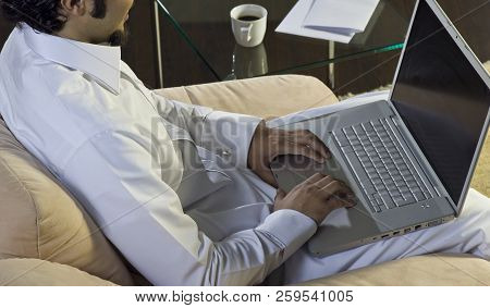 Mideastern Man Using Laptop At Office, With A Cup Of Cofee And Documents On The Side Table