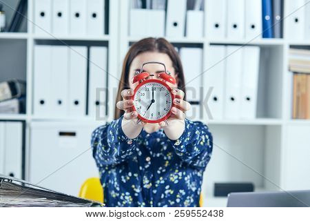 Female Office Worker Holding A Large Red Alarm Clock In Front Of Her Face.