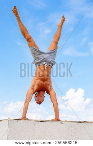 Man Stands On His Hands Against A Beautiful Blue Sky