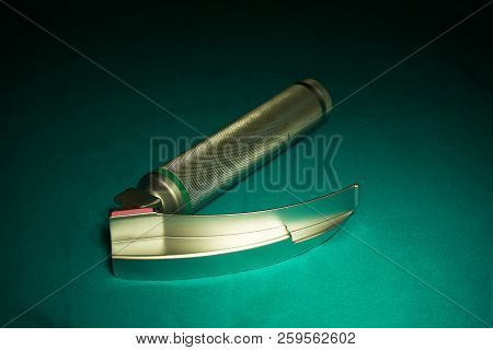 A Silver Laryngoscope On The Green Table And Operating Room Light On The Laryngoscope
