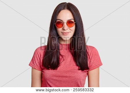 Indoor Shot Of Stylish Brunette Girl Wears Trendy Red Round Sunglasses, Casual T Shirt, Ready To Hav
