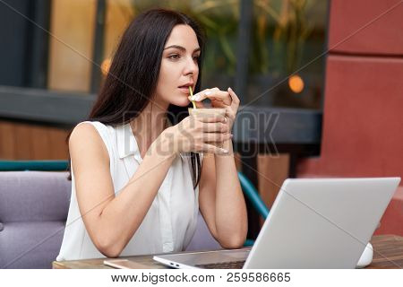 Thoughtful Businesswoman Has Coffee Break In Outdoor Cafeteria, Uses Laptop Computer For Distant Wor