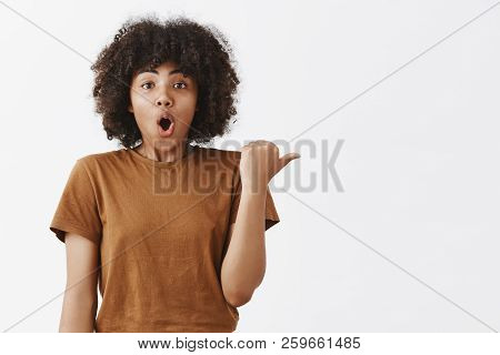 Excited And Stunned Impressed Dark-skinned Girl Witha Afro Hairstyle In Brown Trendy T-shrit Folding