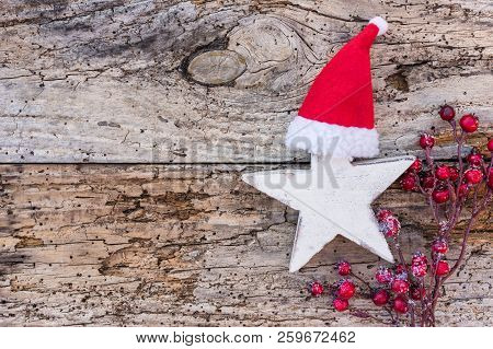 Christmas Or Advent Decoration With Wooden Star Shape, Santa Claus Cap An Red Berries On Wood