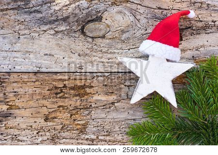 Advent And Christmas Decoration With Star Shape, Red Santa Claus Hat And Green Fir Tree Branch On Wo