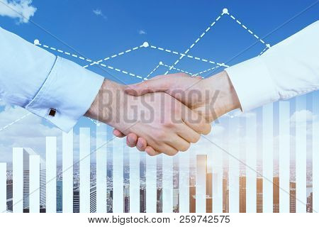 Close Up Of Two Businessmen Shaking Hands Over A Cityscape Background. Graph And Diagrams In The For