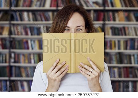 Portrait Of Woman In A Library Face Half-covered By Opened Book, Long Hair. Young College Student Gi
