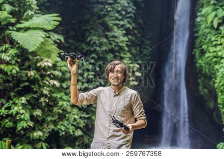 The Man Controls The Drone Against The Background Of The Forest And The Waterfall