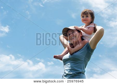 A mãe com uma filha pequena contra o céu