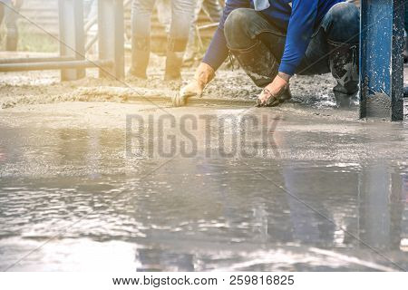 Man Sitting And Using A Wooden Spatula For Cement After Pouring Ready-mixed Concrete On Steel Reinfo