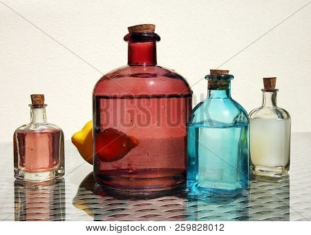 Still Life With Cold Fresh Lemonade, Compote And Lemon Juice In The Small Color Glass Botlles Agains
