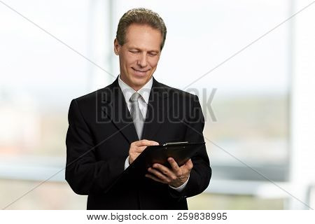 Caucasian Businessman Writing On Clipboard. Mature Man In Formal Wear Making A Note On Black Clipboa