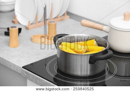 Stewpot With Water And Corn Cobs On Stove In Kitchen