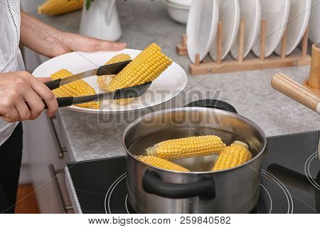 Woman Putting Raw Corn Cob Into Stewpot On Stove, Closeup