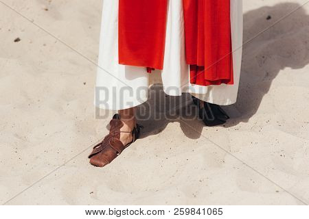 Cropped Image Of Jesus In Robe, Red Sash And Sandals Standing On Sand In Desert