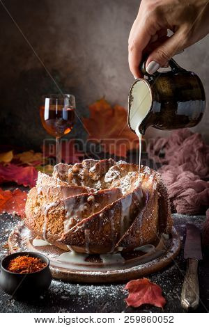 Bundt Cake With Saffron And Rum Covered With White Glaze On Rustic Background With Autumn Decoration